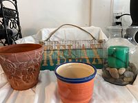 Photo of terracotta flower pot with floral design, orange ceramic pot, wooden 'RELAX' sign, and glass vase with candle and stones