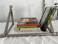 Side view of the metal over-the-door hanging bar with six coffee table books stacked next to it, showing book titles and general size.