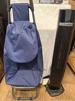 Blue pull cart with fabric bag and black handle next to a Lasko tower heater.