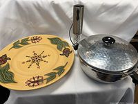 Photo showing the hammered pewter serving dish with glass insert and lid, a large yellow floral ceramic plate, and a stainless steel rechargeable wine cork remover.