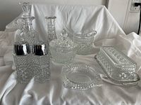 Full view of the crystal set including butter dish, salt and pepper shakers, cream and sugar containers, vinegar bottle, bud vase, and ashtray on white cloth background