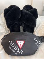 Photo showing the black furry slippers placed behind a black Guess branded crossbody bag with logo printing on the front.