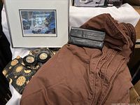 Lot overview showing brown duvet cover, wallet, glass plates with loonies, makeup bags, and framed wolf art.