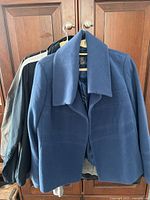 Four medium sized ladies coats and hoodies hanging on hangers. Front coat is blue with wide collar.