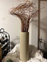 Tall off-white textured heavy ceramic vase with curly brown decorative sticks inside.