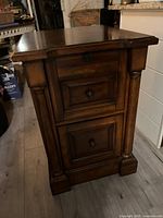 Front side view showing two paneled drawers with knobs, lock on top drawer, and classical column-style accents.