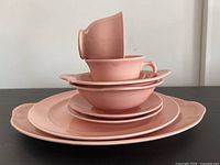 Stack of pink LuRay pastel dishes showing platter, dinner plate, side plate, bowls, saucer, and tea cups in soft pink finish with scalloped edges.