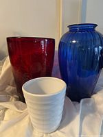 Two large vases, one red and one blue, and one white ceramic flower pot together on white fabric background.