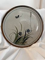 Front view of the signed pottery plate showing overall floral design and butterfly motif