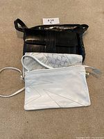 Three vintage purses stacked on carpet: black snake skin purse on top, white and grey eel skin purse and white purse with geometric stitch on bottom.