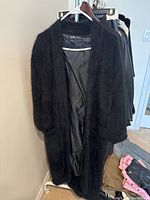 Open view showing long black trench coat with soft textured angora knit exterior, black satin-like lining, and pockets.