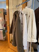 Three reversible jackets hanging on a clothing rack, showing olive green, white, and brown colors, folded collars visible.