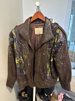 Front view of vintage brown leather bomber jacket with colorful paint splatter design and zip front closure