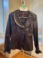 Front view of black leather jacket with shawl collar and button closure.