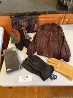 Full lot overview showing handbag, bomber jacket, gloves, and leather finger puppets arranged on table