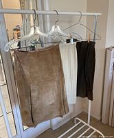 Three skirts hanging on a garment rack: tan leather/skirt and two knit skirts in cream and dark brown