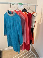 Five vintage mini dresses on hangers displayed on a clothing rack, showing variety of colors and styles.