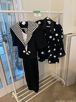 Front view of black polka dot blazer with large white buttons hanging next to dress on rack.