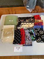 Multiple silk scarves and pashminas folded on a table with various colors and patterns.