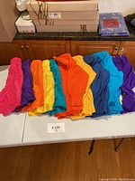 Photo showing a lineup of folded silk shorts and cardigans in various colors on a table.