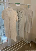 Three vintage-style dresses and romper hung on clothing rack, showing pearlescent silver and white colors and patterns