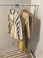 Three vintage clothing items hanging on rack, two sweater dresses and one blouse