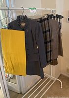View of multiple skirts and a suit jacket hanging on rack, showcasing plaid and solid wool fabrics including yellow and gray pinstripe pieces