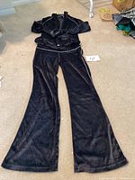 Full view of black velour track suit laid out on carpeted floor, showing jacket and pants together.