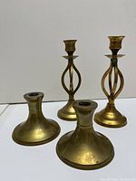 Photo showing two pairs of brass colored candlesticks, one pair short (about 3.5 inches tall) and one pair tall (about 8 inches tall) with a distressed patina finish.