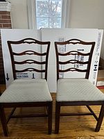 Two dark wood dining chairs with ladderback design and upholstered light beige seats, showing wear and small stains.