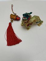 Photo of colorful jeweled dragon trinket box and small fish ornament with red tassel on white background