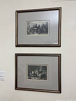 Photo showing two framed black and white prints hung vertically on a wall, each with gray matting and brown frames.