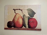Photo shows a printed wall art piece with a large pear, peach, and plum on a neutral brown-beige background with green leaves and a wooden surface base.