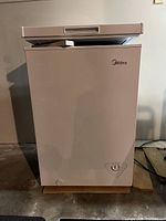 Front view of the white Midea chest freezer with closed lid showing brand logo and control dial at bottom right.