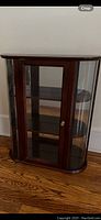 Front view of a dark wood wall cabinet with three internal shelves, glass door, and mirrored back panel.