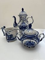 Three pieces of a blue and white Russian tea set including teapot, creamer, and sugar bowl on a white surface