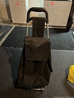 Front view of the metal shopping cart with attached black canvas bag, positioned upright showing padded handle and flap closure of the bag.