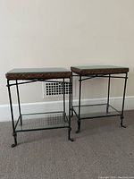 Photo showing two small end tables with iron bases, wicker tops, removable clear glass protective tops and removable glass shelves below. Tables measure approximately 16x11x21 inches.