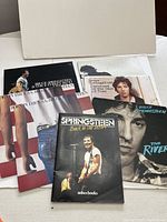 Photo showing a collection of Bruce Springsteen vintage vinyl albums and a booklet laid out on a table. Includes Born in the USA, The River, Darkness on the Edge of Town, and other albums.