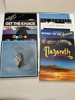 Photo showing 12 vintage vinyl record albums arranged in two rows, titles and artists including Bob Seger, The Knack, Pat Benatar, Devo, Eagles, Nazareth and others.