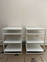 Photo of two matching white metal shelves side by side against a wall on cardboard surface.