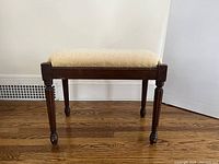 Front view of the wooden bench showing carved legs and gold floral upholstery on the seat.