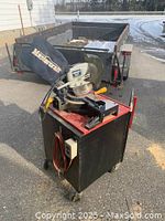Photo of a Mastercraft 10 inch compound mitre saw mounted on a black rolling cabinet outside, showing dust bag and power cord