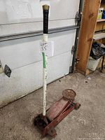 Heavy duty floor jack with red base and white handle, positioned upright in a workshop setting.