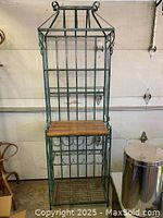 Full view of green metal baker's rack with wood top showing shelving and scroll decorative details.