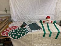 Photo of Christmas-themed table runners, place mats, and Santa Claus plush card holder on a table against a white backdrop.