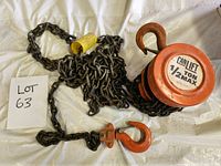 Orange round metal chain hoist with 'CAN LIFT 1/2 TON MAX' label, heavy metal chain and two hooks, one on the hoist and one on the free end.