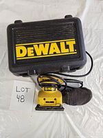 Photo of DeWalt palm sander with attached dust bag alongside black hard carrying case with large yellow DeWalt markings.
