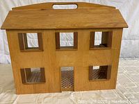 Front view of the doll house showing the wooden exterior with six window openings and carry handle on the roof.