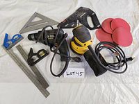 Photo shows the Black & Decker electric drill with power cord, handheld electric sander, four red sanding discs and multiple metal carpentry squares and scriber tools arranged on a white background.